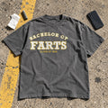 Bachelor of Farts Shirt laid flat in a parking lot