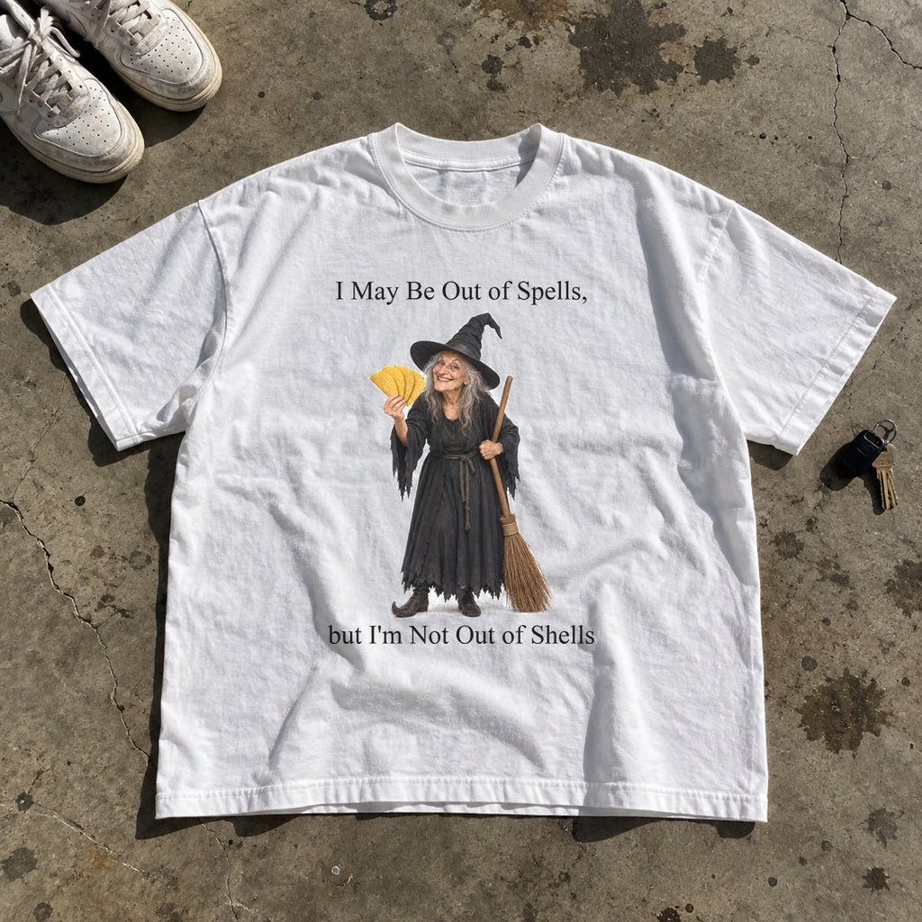 Out of Spells Not Out of Shells Shirt laid flat on a concrete garage floor